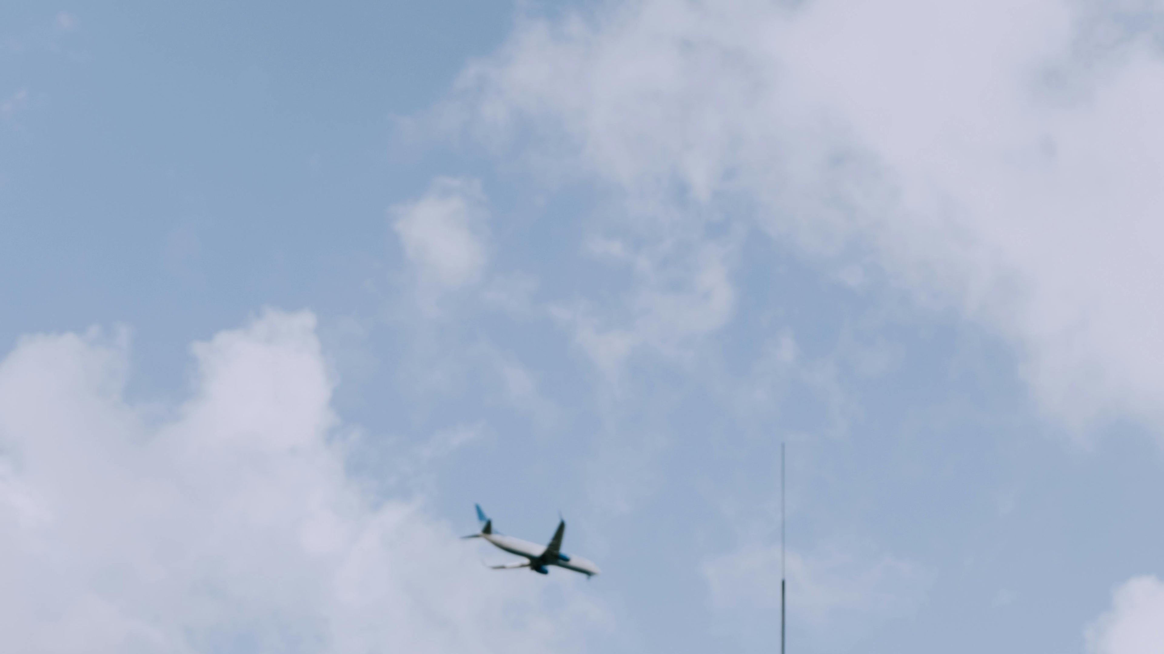 Person with a scarf on their head standing next to a car with an airplane flying in the sky.